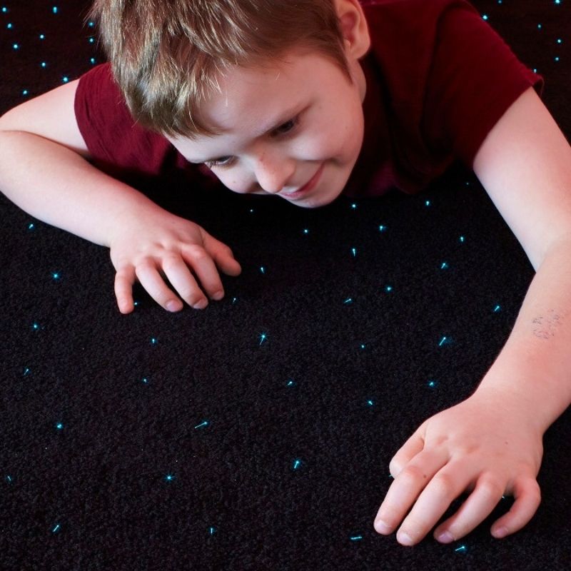 Child crawling on the Experia LED Fibre Optic Star Carpet showing the full-body floor contact with the colour-changing fibre optic lights woven into the 2m x 1m black carpet