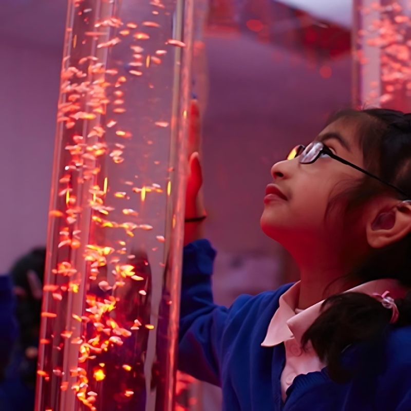 Child actively pressing the 9-button wireless controller to change the Experia Superactive LED Bubble Tube colour, showing interactive colour control of the sensory bubble tube