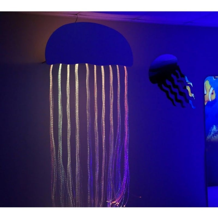 Close-up of the Experia Calming Fiber Optic Jellyfish glowing in purple and blue light, showing the unique tactile underwater sensory component included in the Adventure Room bundle