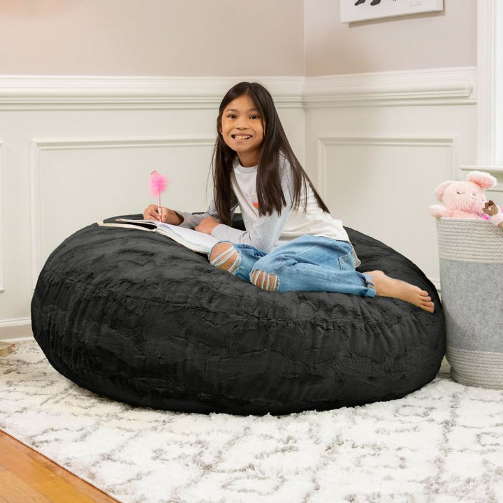A child reading on the Jaxx Cocoon Fur faux fur bean bag chair in Black, styled in a bedroom as everyday kids' seating