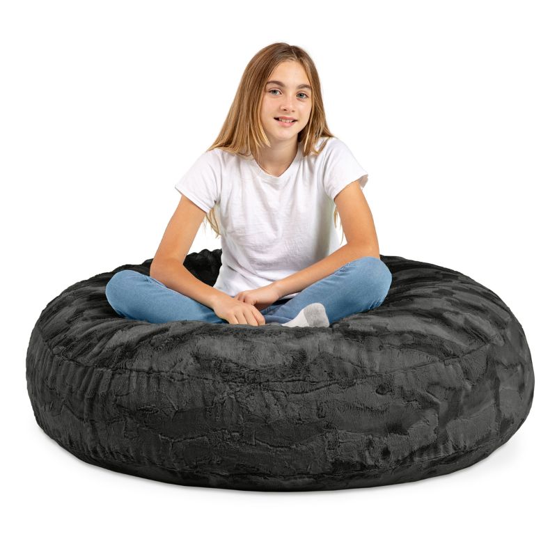 A child sitting cross-legged on the Jaxx Cocoon Fur faux fur bean bag chair in Black, showing its size for kids