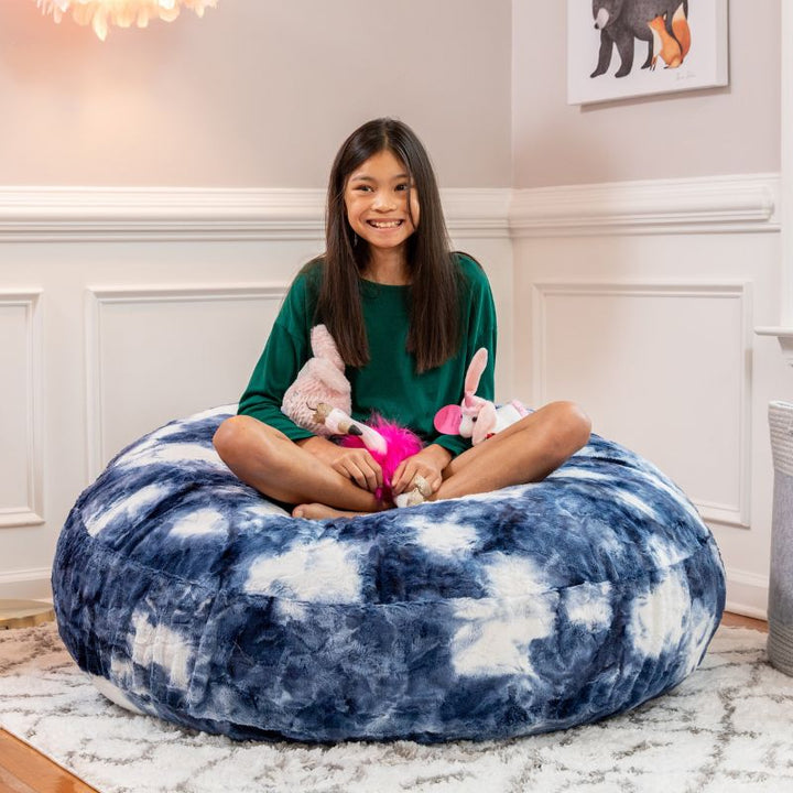 A child sitting cross-legged on the Jaxx Cocoon Fur faux fur bean bag chair in Blueprint, styled in a bedroom setting