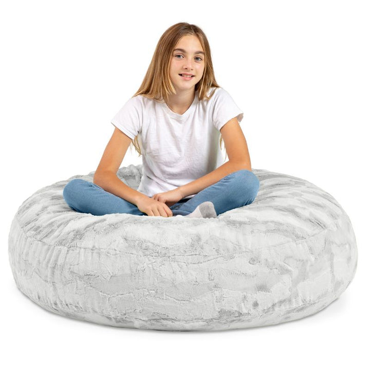 A child sitting cross-legged on the Jaxx Cocoon Fur faux fur bean bag chair in Grey, a neutral seat for kids in any room