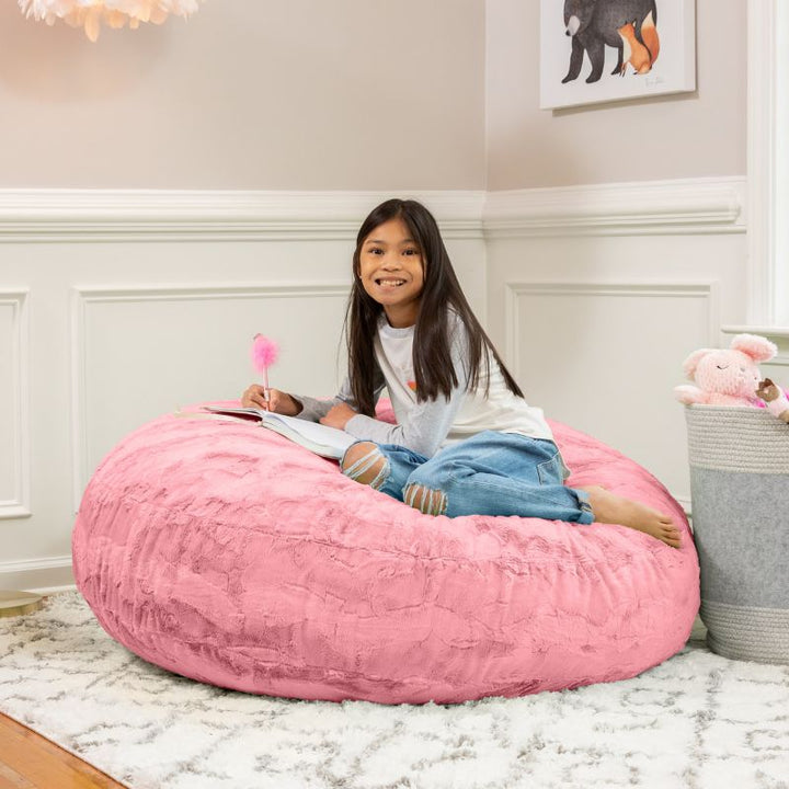 A child reading on the Jaxx Cocoon Fur faux fur bean bag chair in Pink, styled in a bedroom as everyday kids' seating