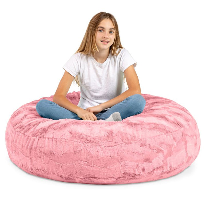 A child sitting cross-legged on the Jaxx Cocoon Fur faux fur bean bag chair in Pink, everyday sensory seating for kids