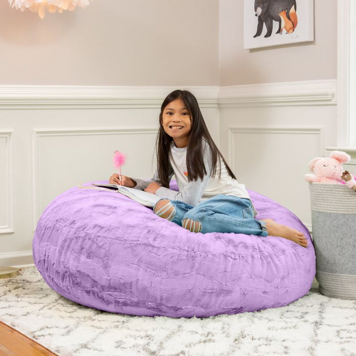 A child reading on the Jaxx Cocoon Fur faux fur bean bag chair in Purple, styled in a bedroom as everyday kids' seating