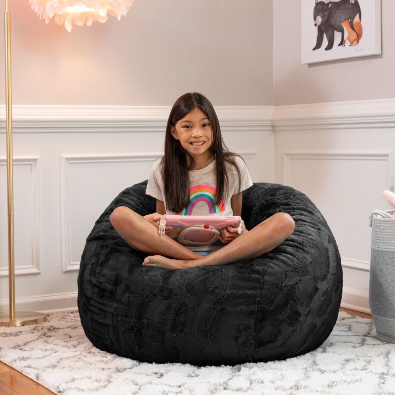 Girl relaxing on the Jaxx Saxx faux fur bean bag chair in Black in a bedroom setting, a soft tactile sensory seat for kids