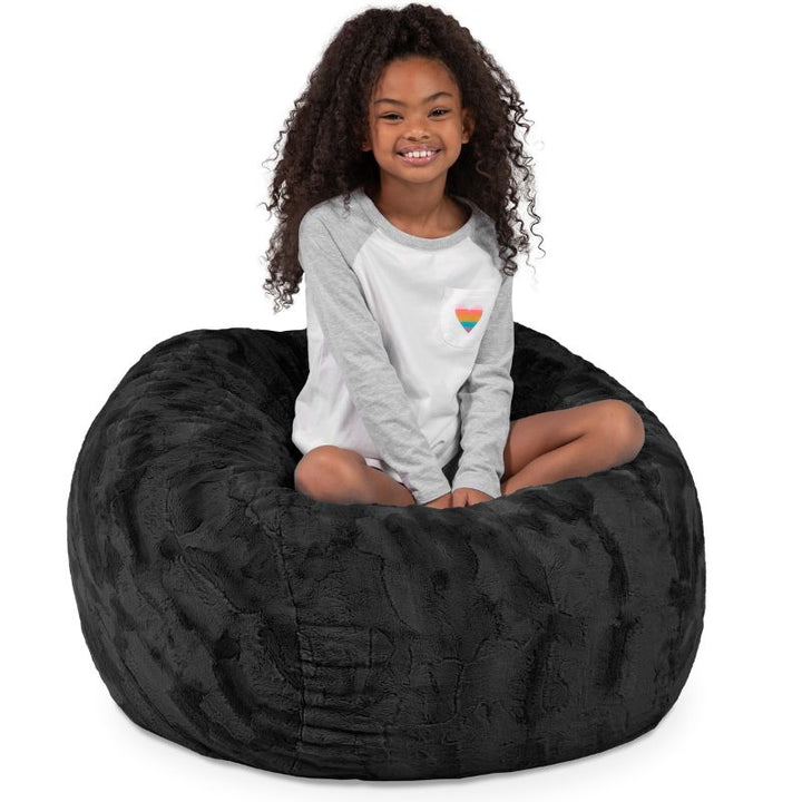 Child seated in the Jaxx Saxx faux fur bean bag chair in Black, a soft tactile sensory seat for kids