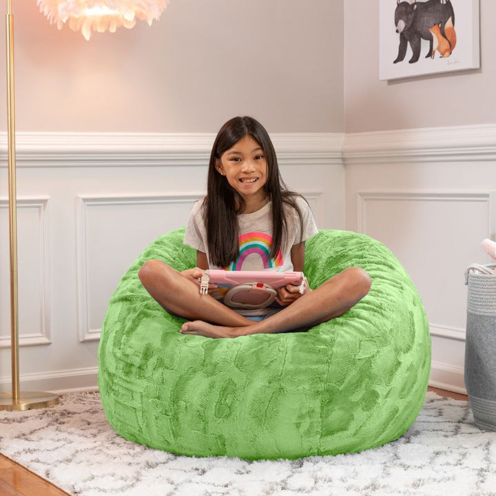 Girl relaxing on the Jaxx Saxx faux fur bean bag chair in Green in a bedroom setting, a soft tactile sensory seat for kids