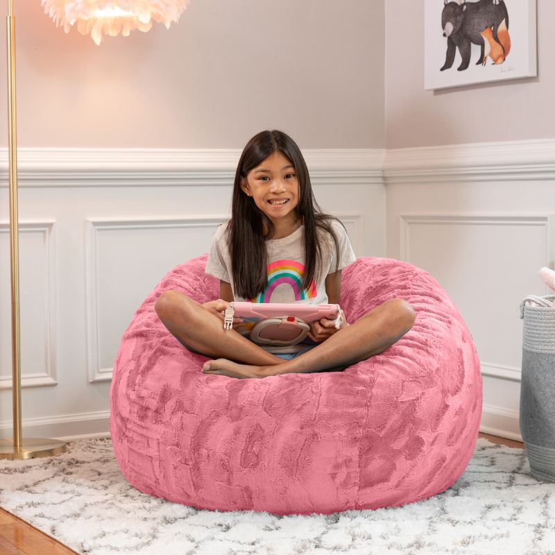 Girl relaxing on the Jaxx Saxx faux fur bean bag chair in Pink in a bedroom setting, a plush tactile sensory seat for kids