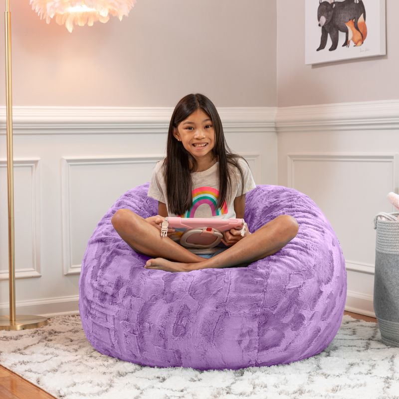 Girl relaxing on the Jaxx Saxx faux fur bean bag chair in Purple in a bedroom setting, a soft tactile sensory seat for kids