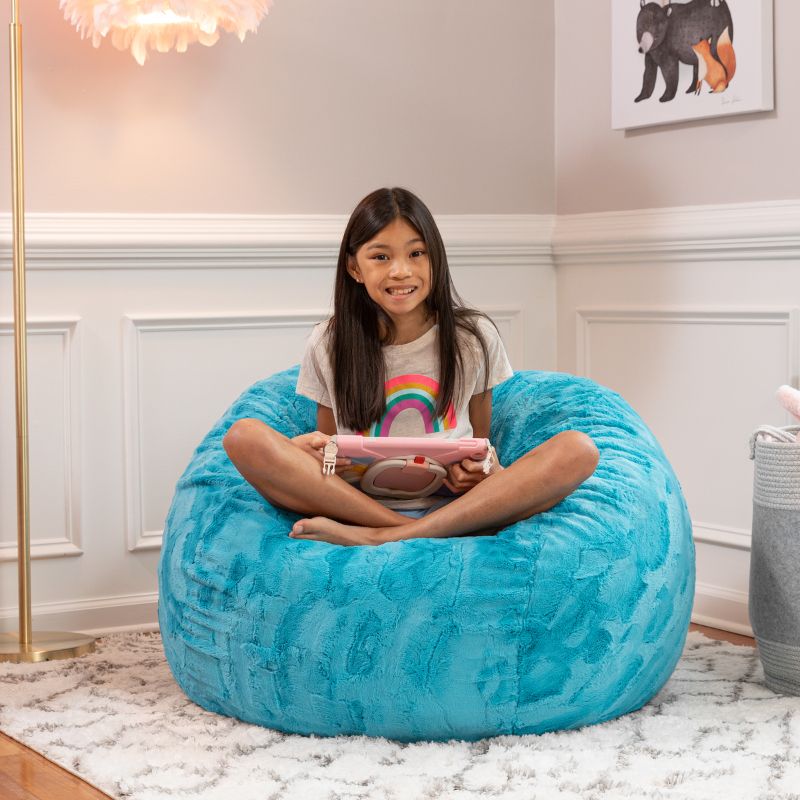 Girl relaxing on the Jaxx Saxx faux fur bean bag chair in Teal in a bedroom setting, a soft tactile sensory seat for kids