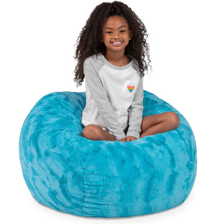 Child seated in the Jaxx Saxx faux fur bean bag chair in Teal, a soft tactile sensory seat for kids