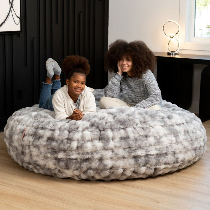 Big Snuggler by Raven-Symone faux fur bean bag lounger in Phantom Gray with two people relaxing together