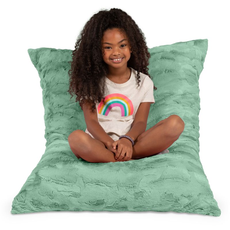 Girl seated cross-legged on the CrashPuff by Raven-Symoné faux fur floor lounger in Spearmint