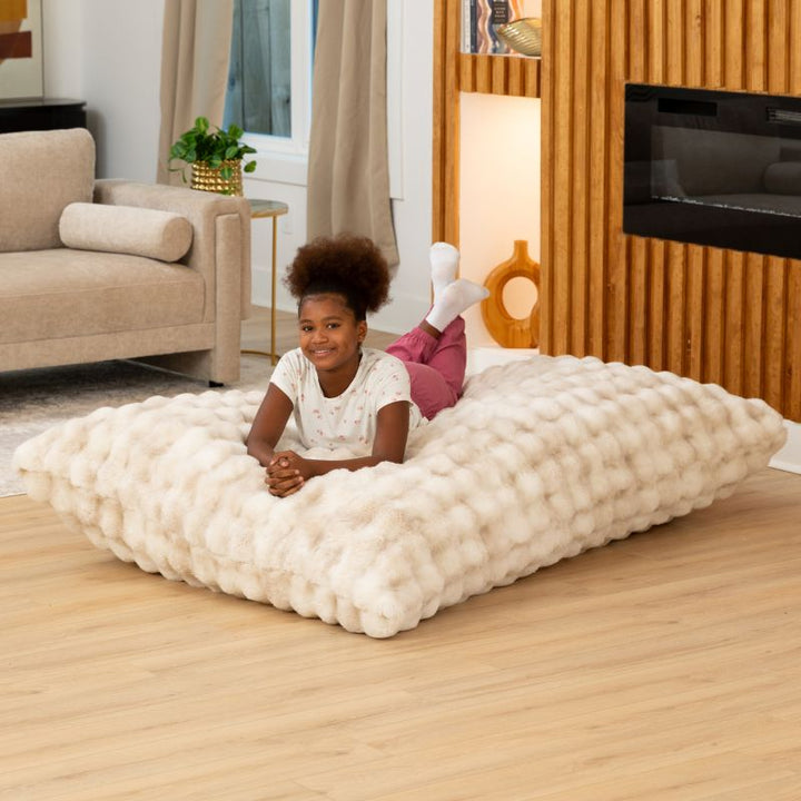 Child relaxing on the Raven-Symoné LoungePuff faux fur floor lounger in Phantom Cream