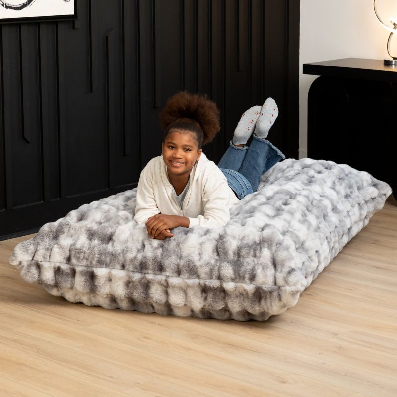 Child relaxing on the Raven-Symoné LoungePuff faux fur floor lounger in Phantom Grey