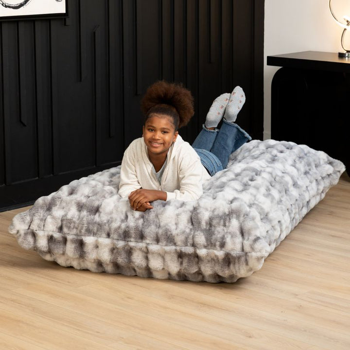 Child relaxing on the Raven-Symoné LoungePuff faux fur floor lounger in Phantom Grey
