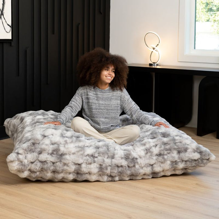 Teen sitting cross-legged on the Raven-Symoné LoungePuff faux fur floor lounger in Phantom Grey