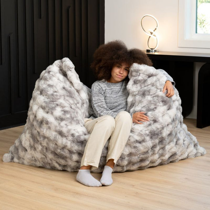 Two children sitting together in the Raven-Symoné LoungePuff faux fur floor lounger in Phantom Grey
