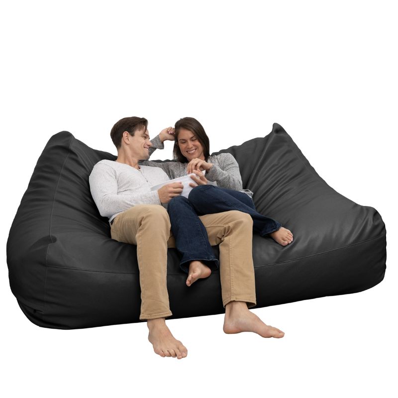 Two people relaxing on the Jaxx Lozia faux leather loveseat in black, a two-seat classroom soft seating option