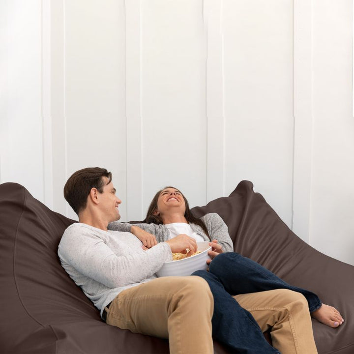 A couple sharing popcorn on the Jaxx Lozia faux leather loveseat in chocolate, easy-clean waiting room seating