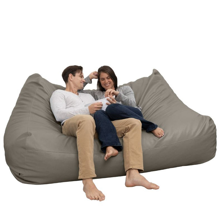 Two people relaxing on the Jaxx Lozia faux leather loveseat in gun metal, a wipeable loveseat for offices
