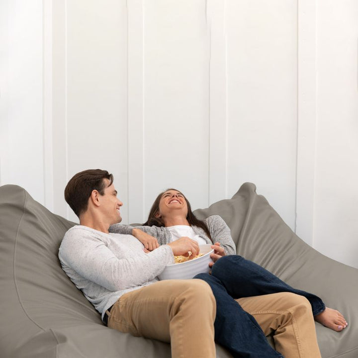 A couple sharing popcorn on the Jaxx Lozia faux leather loveseat in gun metal, a wipeable loveseat for offices