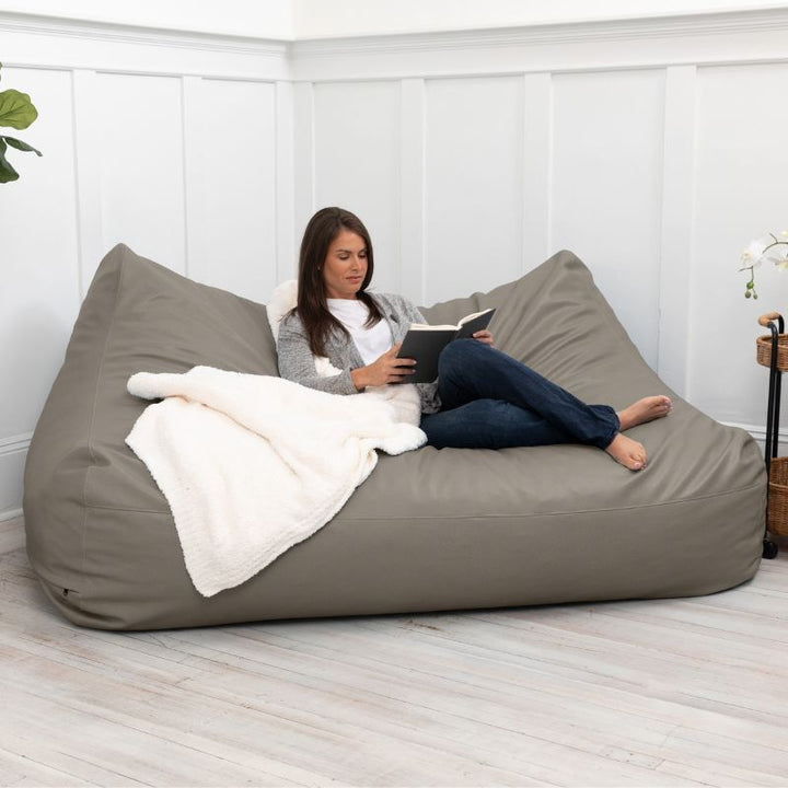 A woman reading on the Jaxx Lozia faux leather loveseat in gun metal, a wipeable loveseat for offices