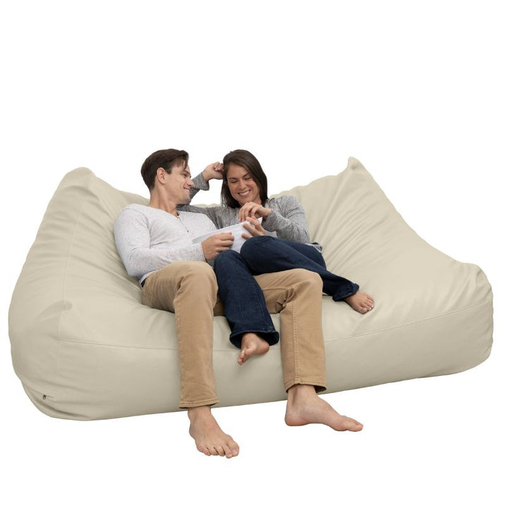 Two people relaxing on the Jaxx Lozia faux leather loveseat in natural beige, classroom soft seating