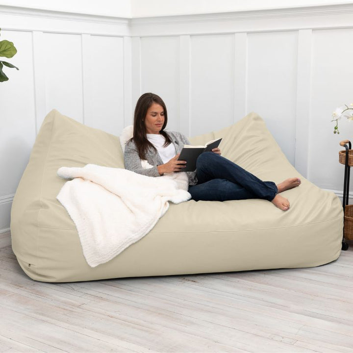 A woman reading on the Jaxx Lozia faux leather loveseat in natural beige, classroom soft seating