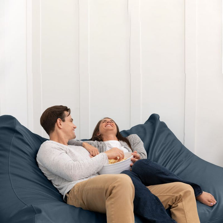 A couple sharing popcorn on the Jaxx Lozia faux leather loveseat in oxford blue, two-seat waiting room seating