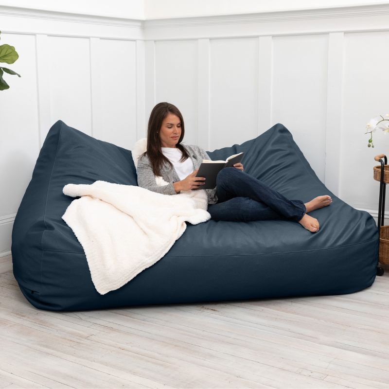 A woman reading on the Jaxx Lozia faux leather loveseat in oxford blue, two-seat waiting room seating