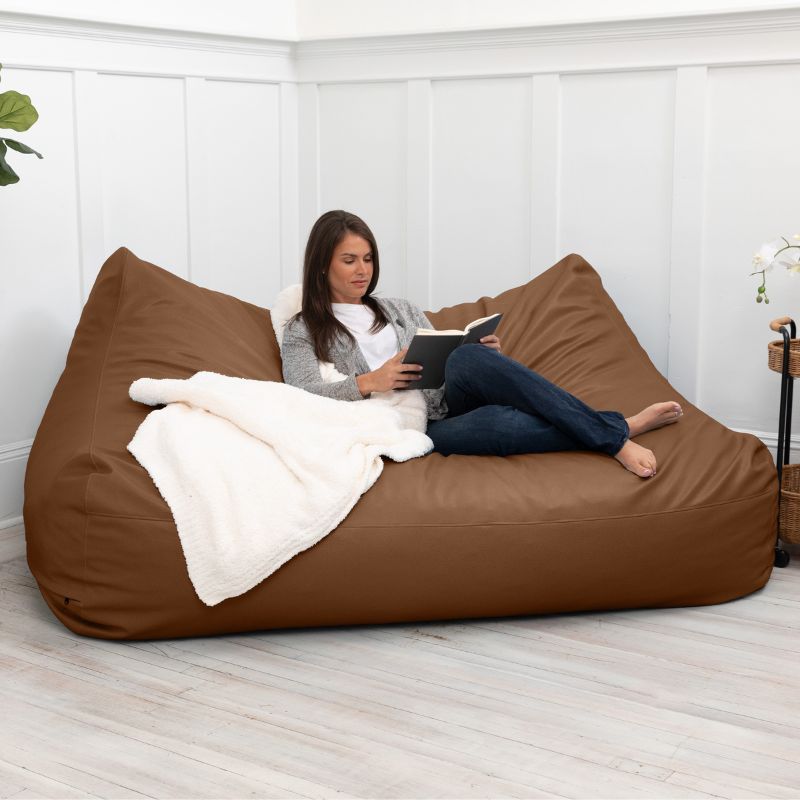 A woman reading on the Jaxx Lozia faux leather loveseat in walnut, easy-clean soft seating for reception areas
