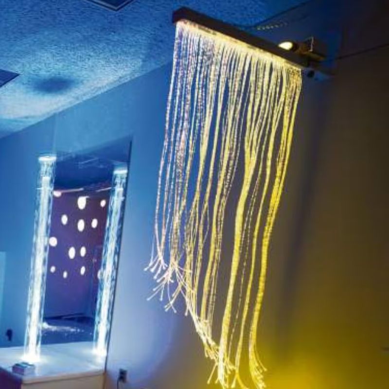 TFH Fiber Optic Curtain mounted on an adjustable wall bracket, glowing gold in a calming sensory room setting