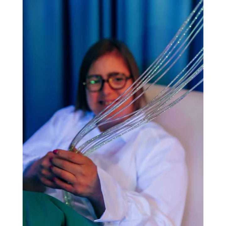 Close up of hands holding the illuminated strands of the TFH Fibre Optic Curtain, showing the tactile texture of this sensory room light