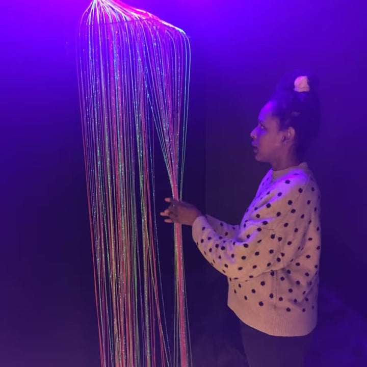 A woman gently touches the glowing strands of the TFH Fibre Optic Curtain Wall Mount during tactile sensory play