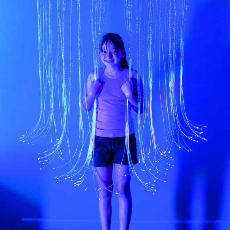 A child standing among the glowing strands of the TFH Fibre Optic Curtain, exploring the tactile and visual sensory play this fibre optic curtain offers