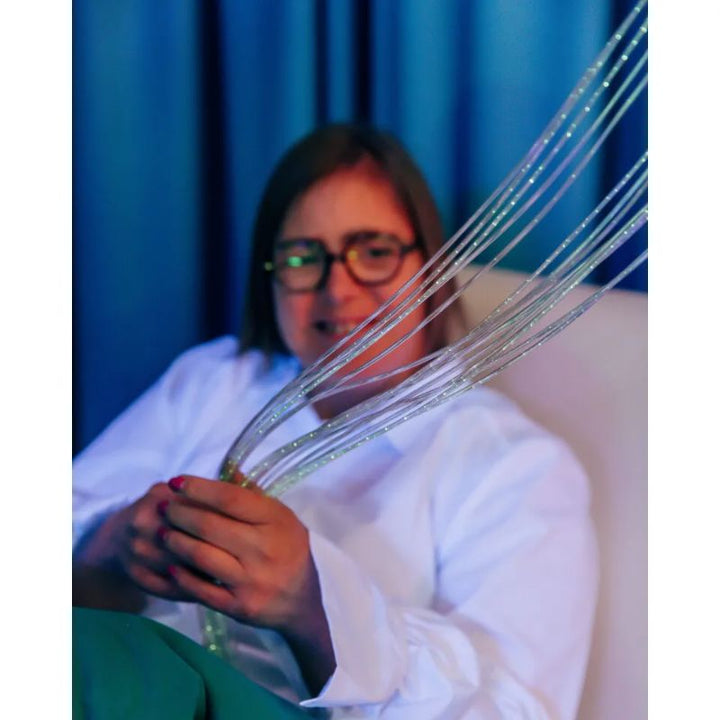 Woman holding a bundle of sparkling TFH Standard Fibre Optic Tails with Light Source, safe-to-touch fibre optic strands for multi-sensory room relaxation
