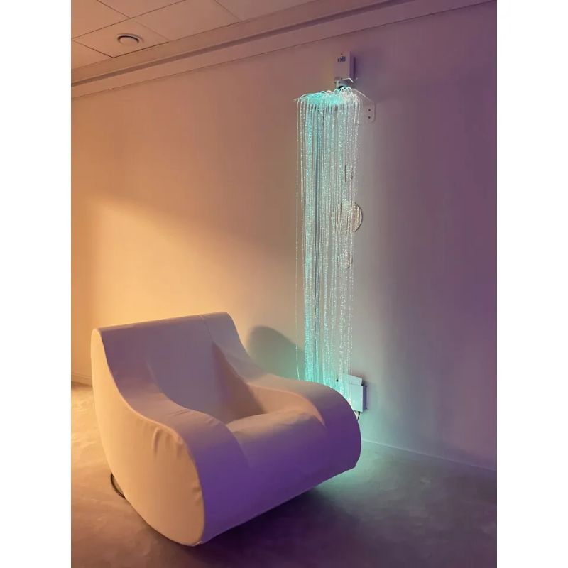 TFH Standard Fibre Optic Tails with Light Source cascading down a wall beside a soft rocking chair, a fibre optic sensory light for calm sensory room spaces