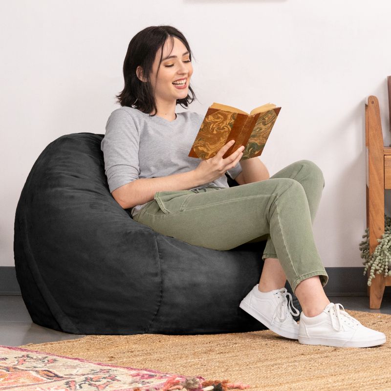 Woman reading a book in a Black microsuede Jaxx Saxx 3ft foam bean bag chair, a cozy reading nook seat that moulds to the body