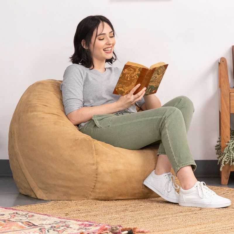 Woman curled up with a book in a Camel microsuede Jaxx Saxx 3ft foam bean bag chair, supportive seating for calm corners
