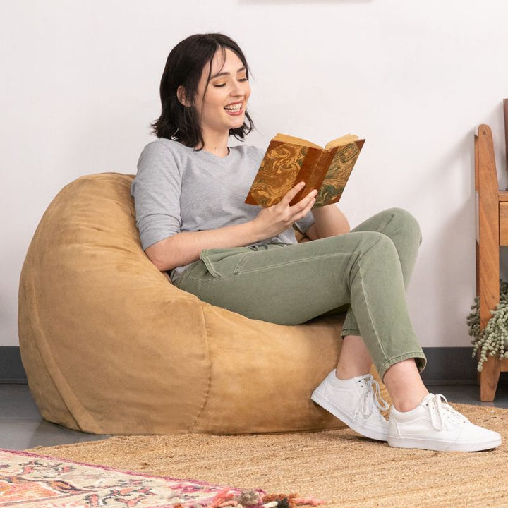Woman curled up with a book in a Camel microsuede Jaxx Saxx 3ft foam bean bag chair, supportive seating for calm corners