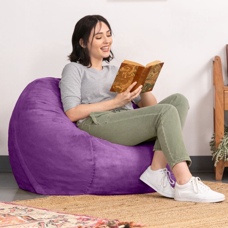 Smiling reader in a Grape microsuede Jaxx Saxx 3ft foam bean bag chair, a supportive round bean bag chair for downtime