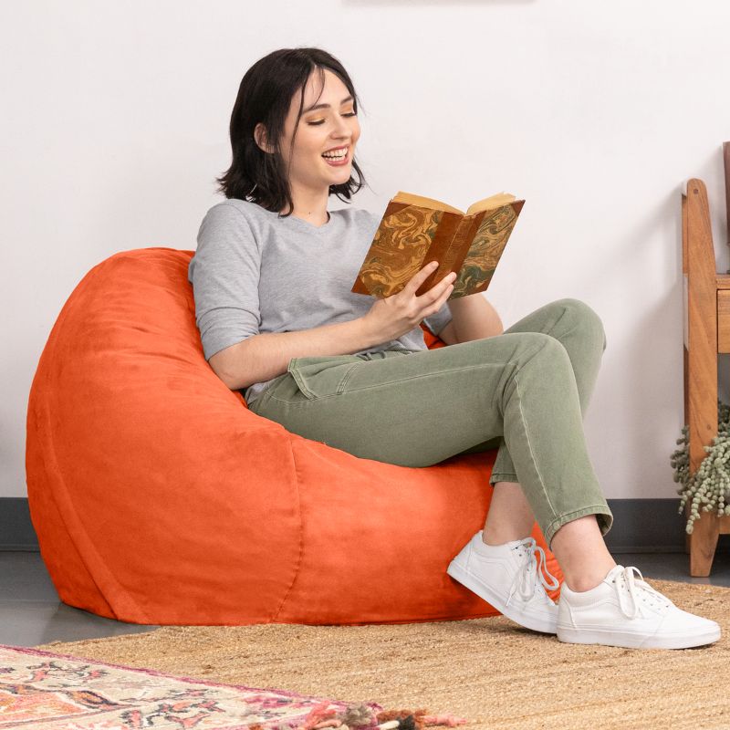 Reader curled up in an Orange microsuede Jaxx Saxx 3ft foam bean bag chair, a supportive seat for quiet reading time