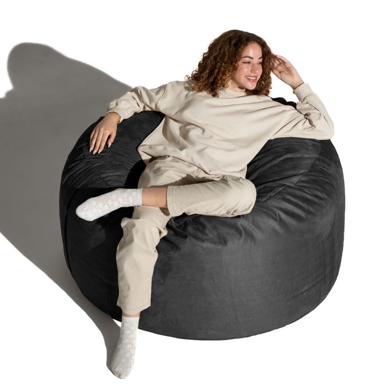 Woman lounging across a Black microsuede Jaxx Saxx 4ft foam bean bag chair, a round bean bag chair roomy enough for adults