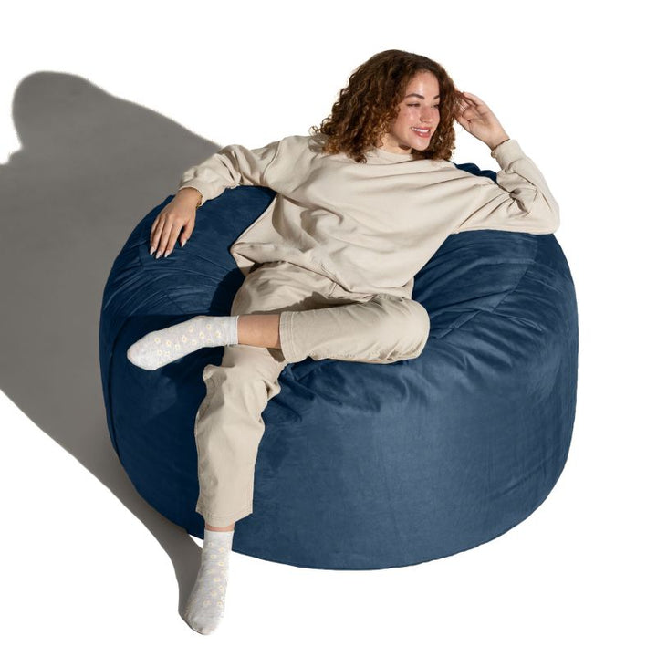 Woman relaxing across a Navy microsuede Jaxx Saxx 4ft foam bean bag chair, calm corner seating that moulds to the body