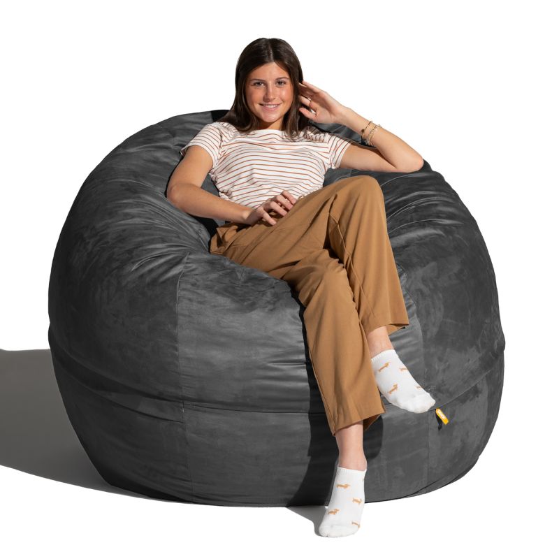 Young woman sitting in a Black microsuede Jaxx Saxx 5ft foam bean bag chair, a large bean bag chair that wraps around the body