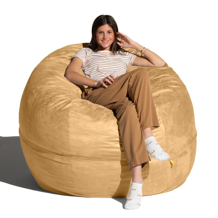 Smiling young woman relaxing in a Camel microsuede Jaxx Saxx 5ft foam bean bag chair, oversized seating for family rooms