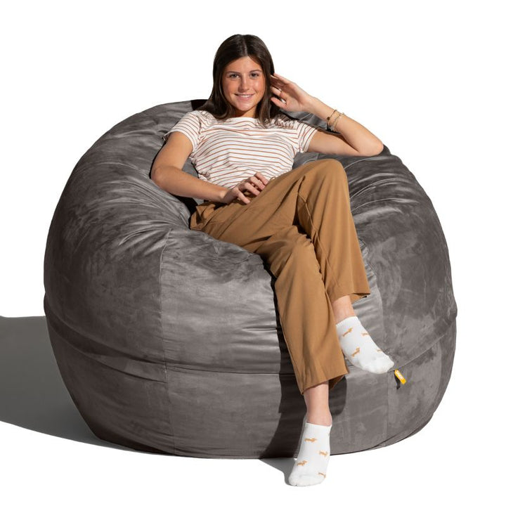 Young woman seated upright in a Charcoal microsuede Jaxx Saxx 5ft foam bean bag chair, showing the scale of this large bean bag chair